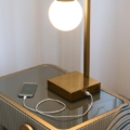 Stolik nocny Scappini Home Away, szary, z jedną szufladą, blat z lakierowanego szkła, wykończenie mosiężne, wyściełany ekoskórą.